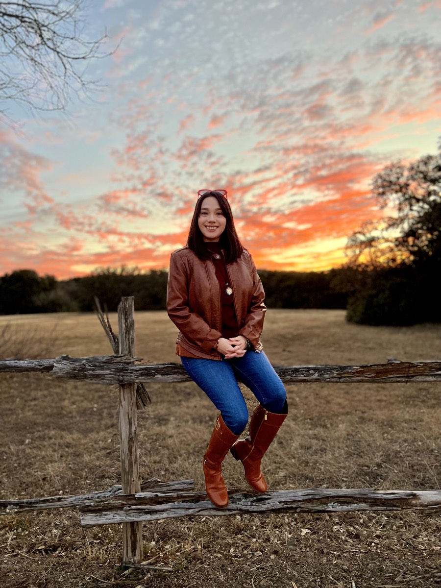 Sarah, Licensed Professional Counselor Associate, seated on a wooden fence at sunset in the Texas Hill Country